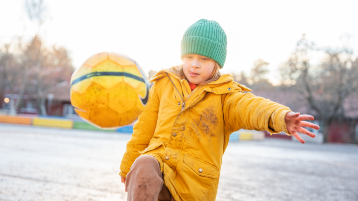 En pojke som dribblar med en fotboll på en skolgård