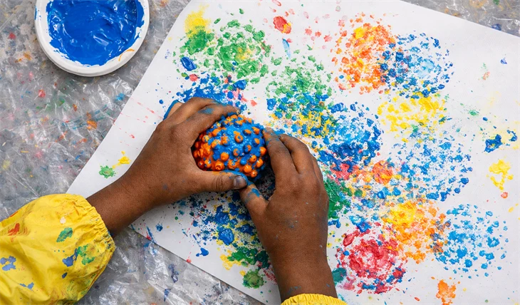 En elev målar med en boll, genom att doppa den i färg och sedan trycka den mot ett papper.