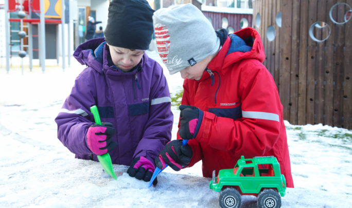 Två barn gräver med små spadar i snön.