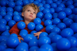Ett barn ligger i ett bollhav med blå bollar och tittar upp mot taket.