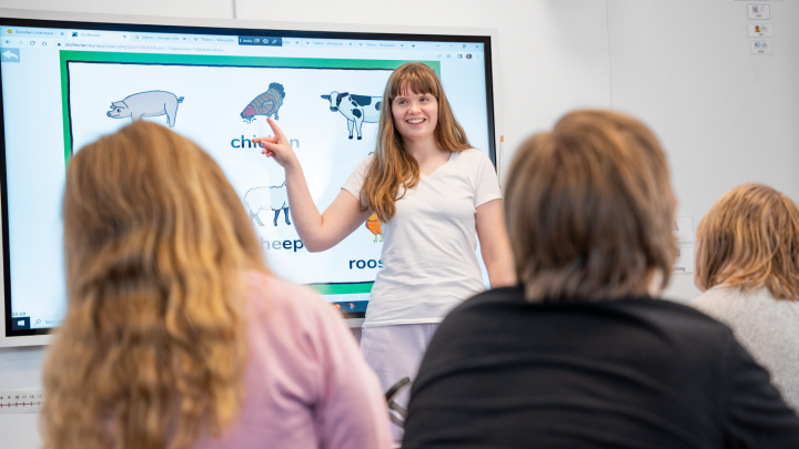 Bilden visar en lärare som pratar med klassen och pekar på bildstöd på en skärm.