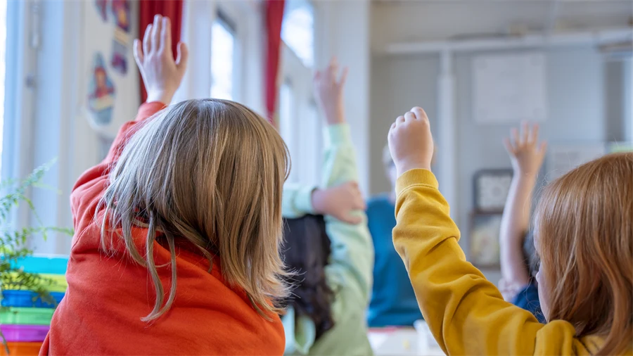 Elever i ett klassrum som räcker upp händerna i luften