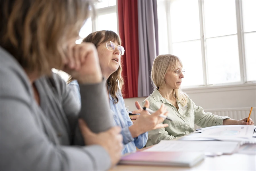 Tre specialpedagoger sitter samlade vid ett bord och konverserar. Personen i mitten gestikulerar med händerna.
