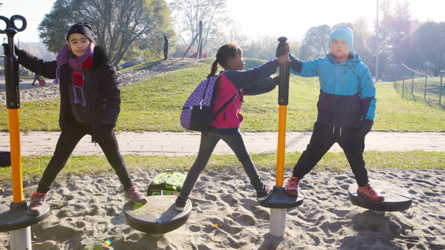 Tre skolbarn på en lekplats som balanserar på en hinderbana