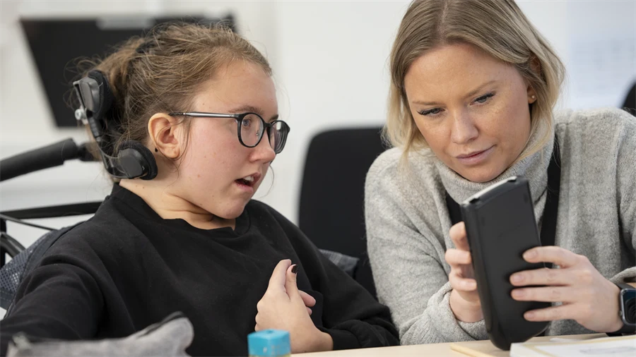 Bilden visar en elev och en vuxen person som tittar på en mobiltelefon tillsammans.