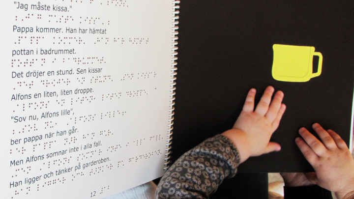 Barnhänderna rör i en punktskriftsbok.