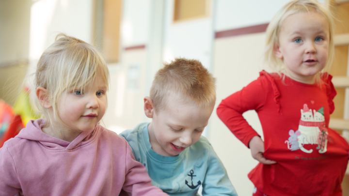 De tre barnen leker med någonting utanför bild. Ett barn tittar in i kameran.